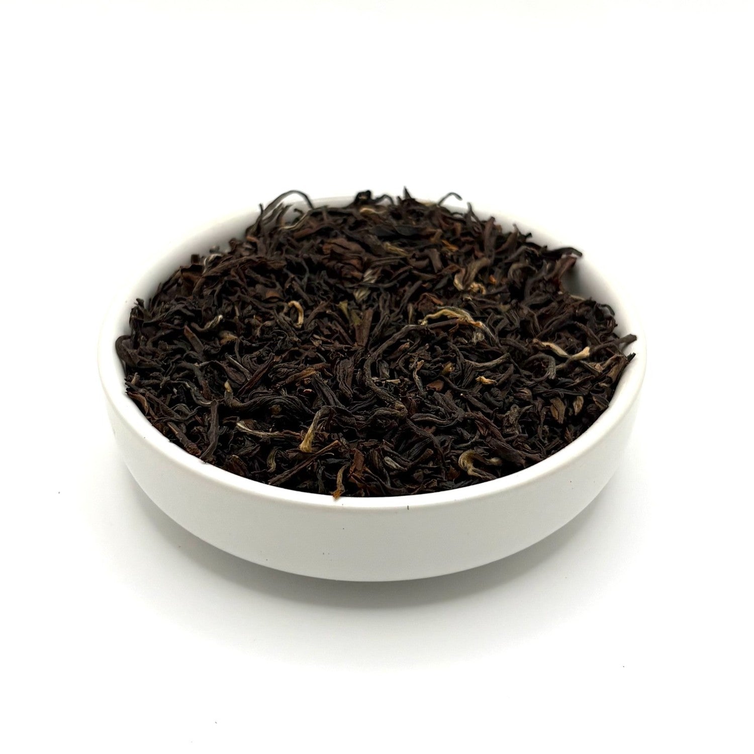 Angled view of dark brown Mountain Copper Oolong tea leaves with golden tips in a white bowl