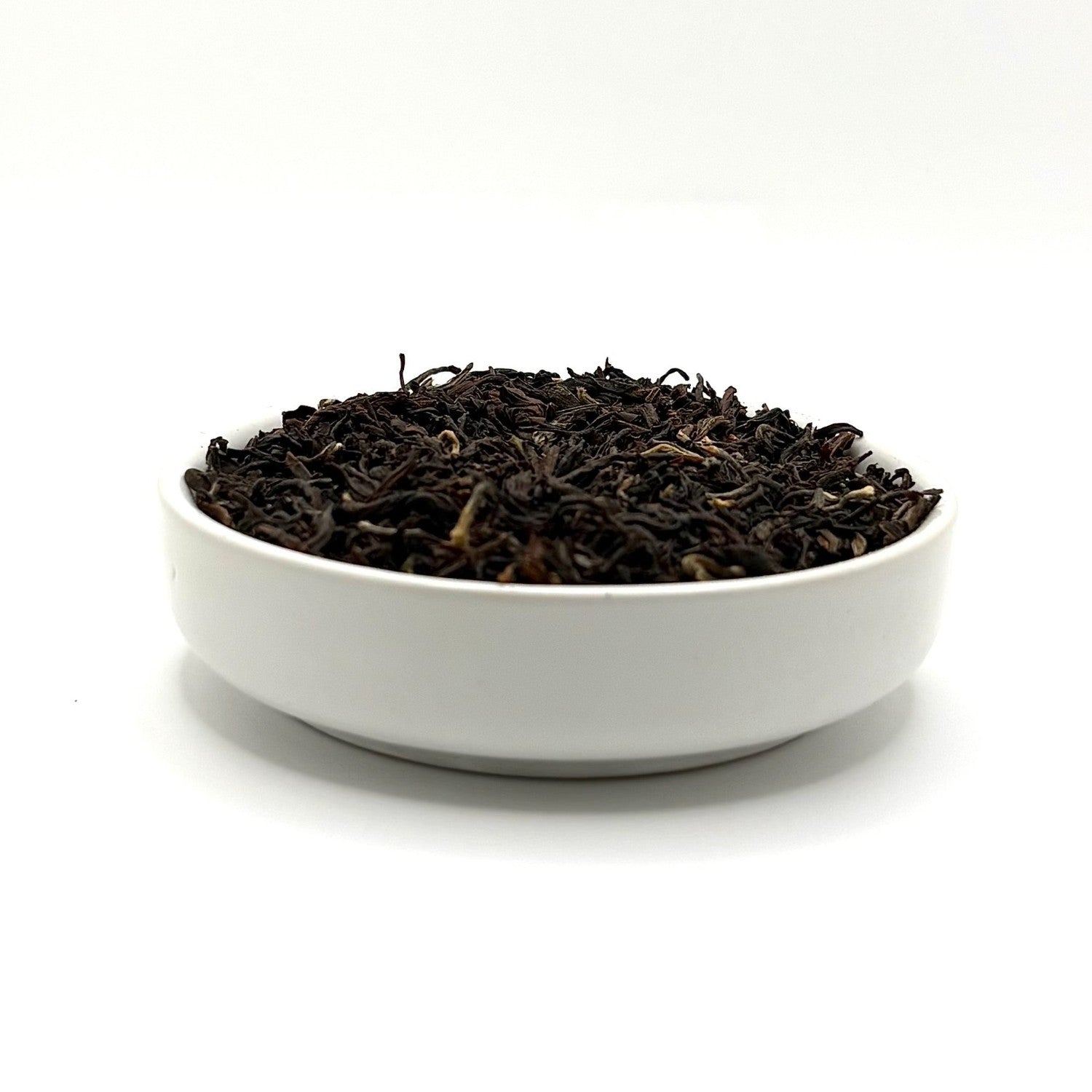 Side view of loose Mountain Copper Oolong tea leaves in a white ceramic bowl on a clean white background